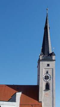 Foto des oberen Bereichs eines Kirchturmes mit Uhr und Spitzhelm.