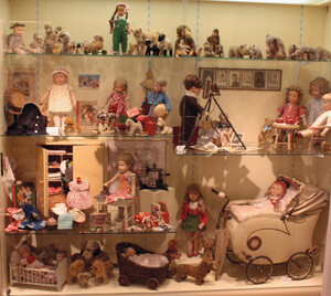 Blick in eine Vitrine mit vielen ausgestellten historischen Puppen und Puppenzubehör.